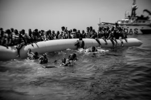Flüchtlingsboot voller Menschen. Im Hintergrund MOAS Rettungsschiff. Foto: Christian Werner / Zeitenspiegel